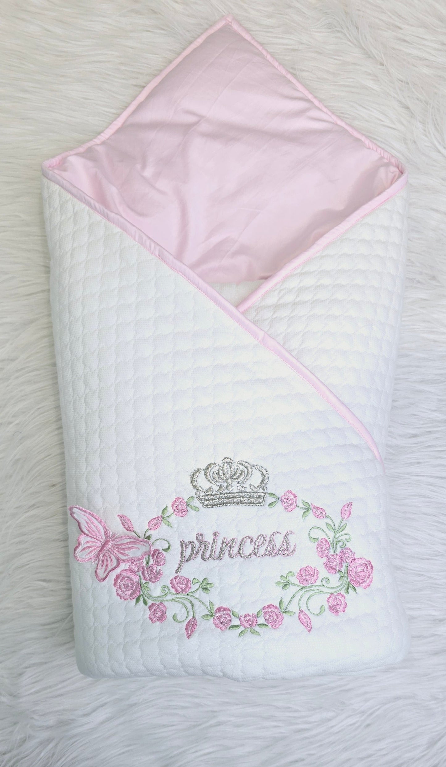 A white and pink baby wrap with 'princess' written in cursive and floral patterns around it, displayed on a white furry surface.