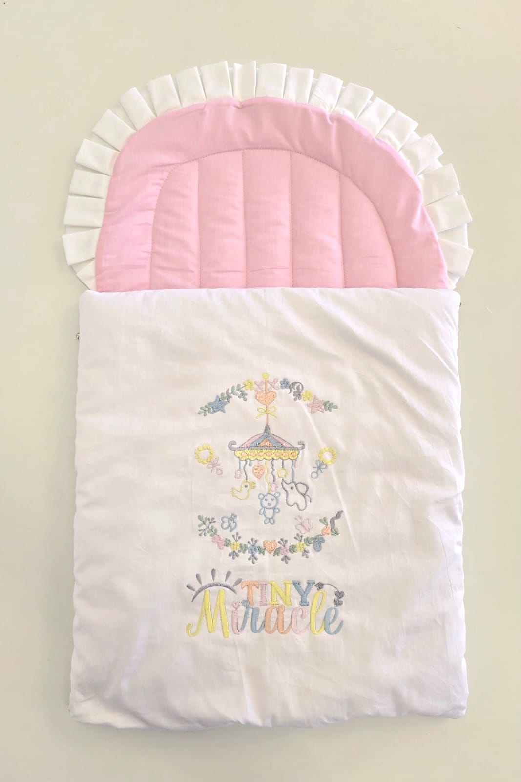 Baby sleeping bag with pink hood and carousel design on a beige background