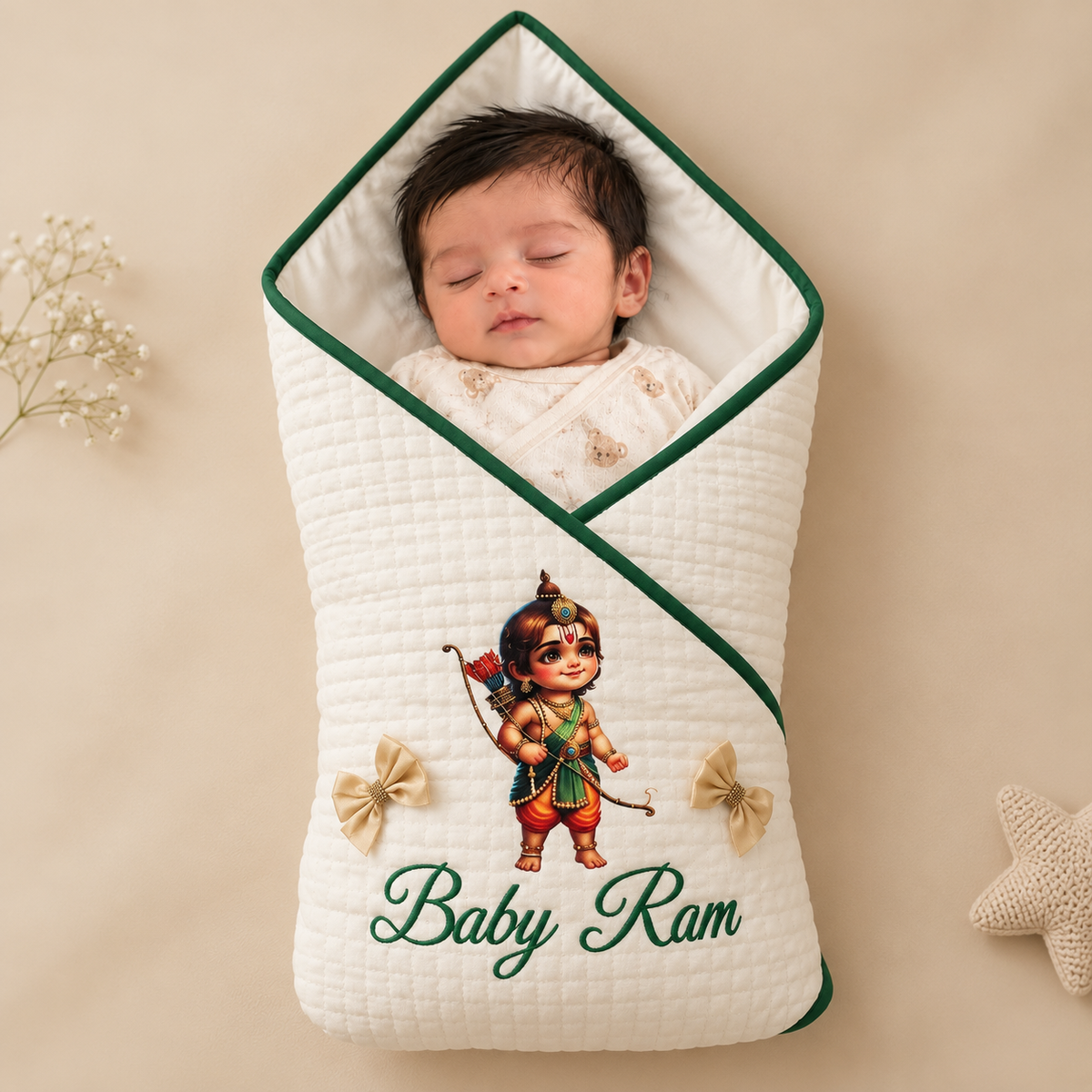 A sleeping newborn baby wrapped in a quilted cream swaddle wrap with green trim, featuring an embroidered illustration of Lord Krishna and the text 'Baby Ram'.