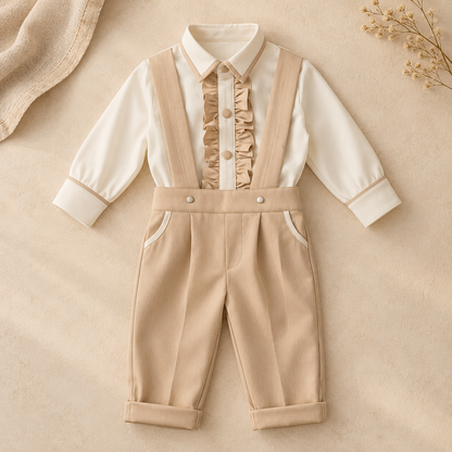 A baby boy's two-piece outfit featuring a cream long-sleeve collared shirt with a ruffled front placket and beige suspenders over matching beige trousers, laid flat on a beige textured background with decorative dried flowers.
