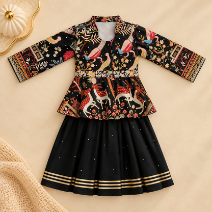 A traditional Indian girl's outfit consisting of a black long-sleeve top with colorful folk art patterns and a matching black flared skirt with gold stripes, laid flat on a beige background.