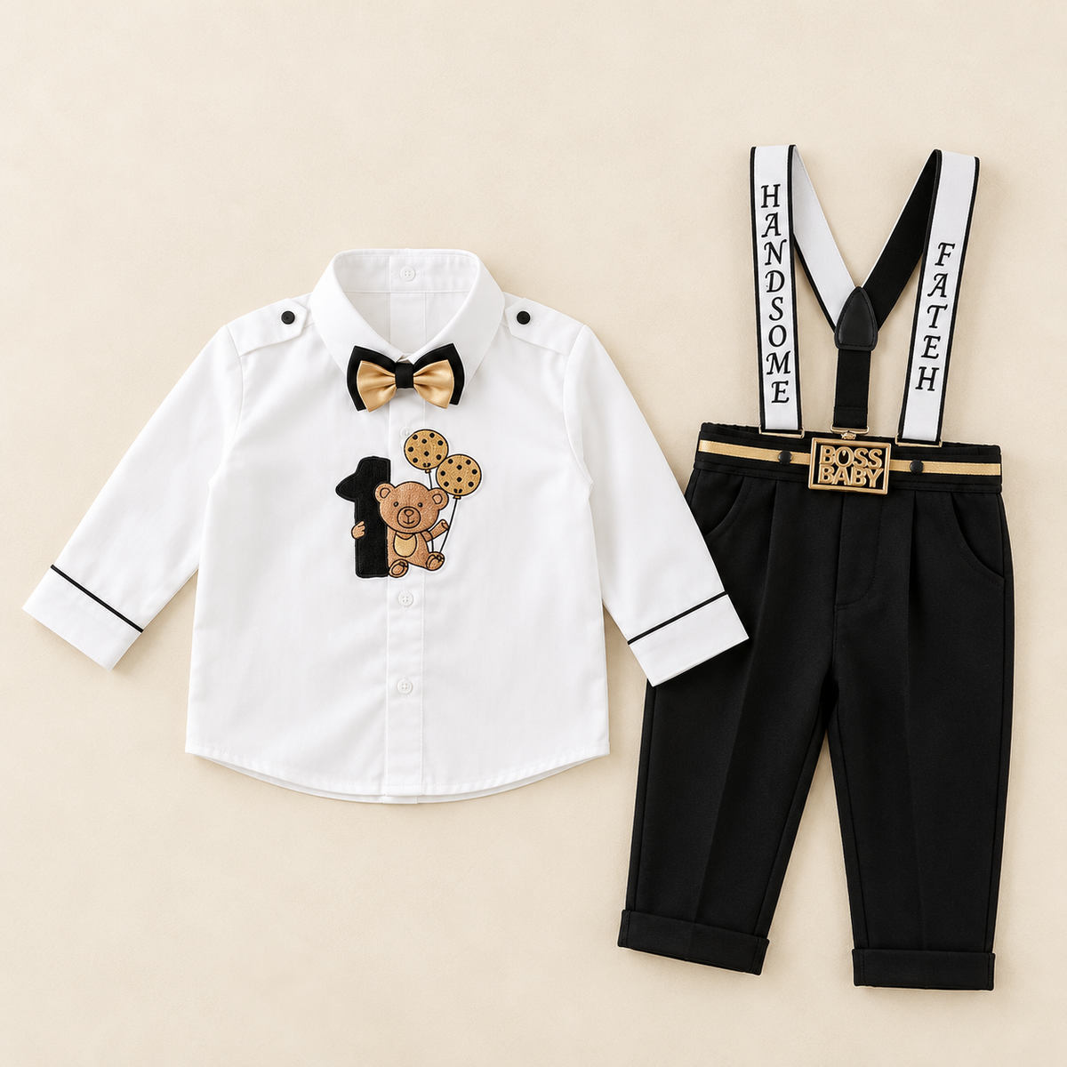 A toddler boy's formal outfit set laid flat on a light beige background, featuring a white long-sleeve shirt with black trim, a black bow tie with a gold center, black pants with white suspenders that read 'HANDSOME' and 'FAITH', and a gold belt with a decorative buckle.