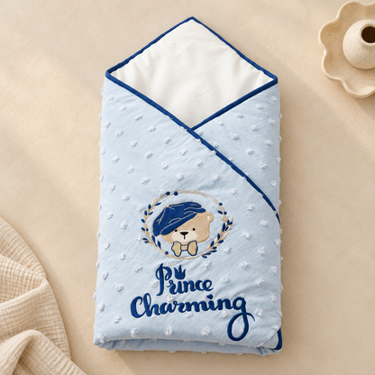 A light blue minky dot swaddle blanket with a teddy bear graphic and the text 'Prince Charming' on a beige background.