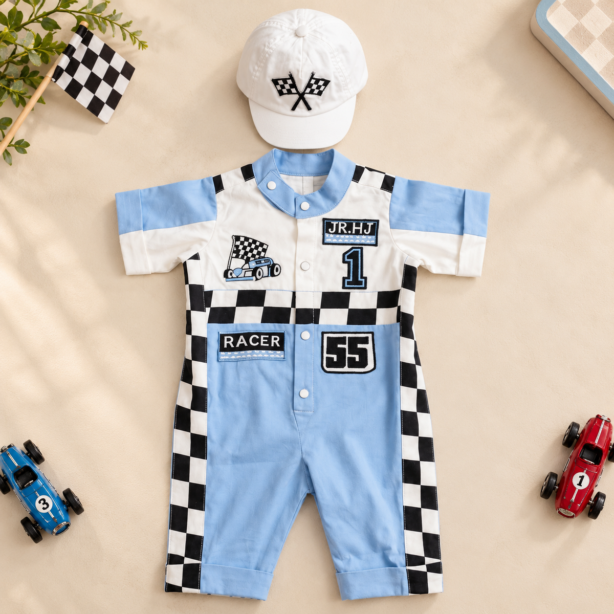 A baby short-sleeve romper and matching cap laid flat on a beige surface. The romper is light blue and white with black-and-white checkered side panels and racing graphics, including the number 55 and patches reading JR.
