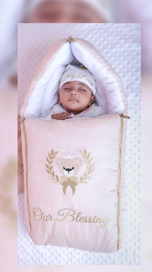 A baby cuddled in a beige receiving baby nest with embroidery detailing and customized text .