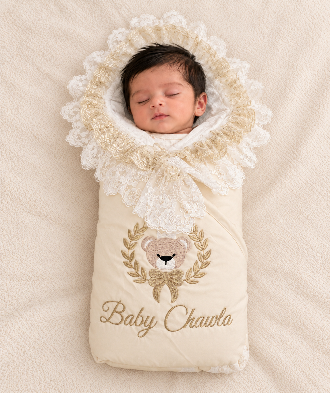 A sleeping newborn baby wrapped in a cream-colored personalized baby swaddle blanket with lace trim and an embroidered teddy bear design. The blanket features the custom name 'Baby Chawla' in gold script.