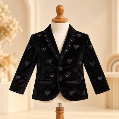 A black velvet boys' blazer with embroidered silver hearts and lace trim on the collar, displayed on a cream mannequin torso with a wooden neck cap.