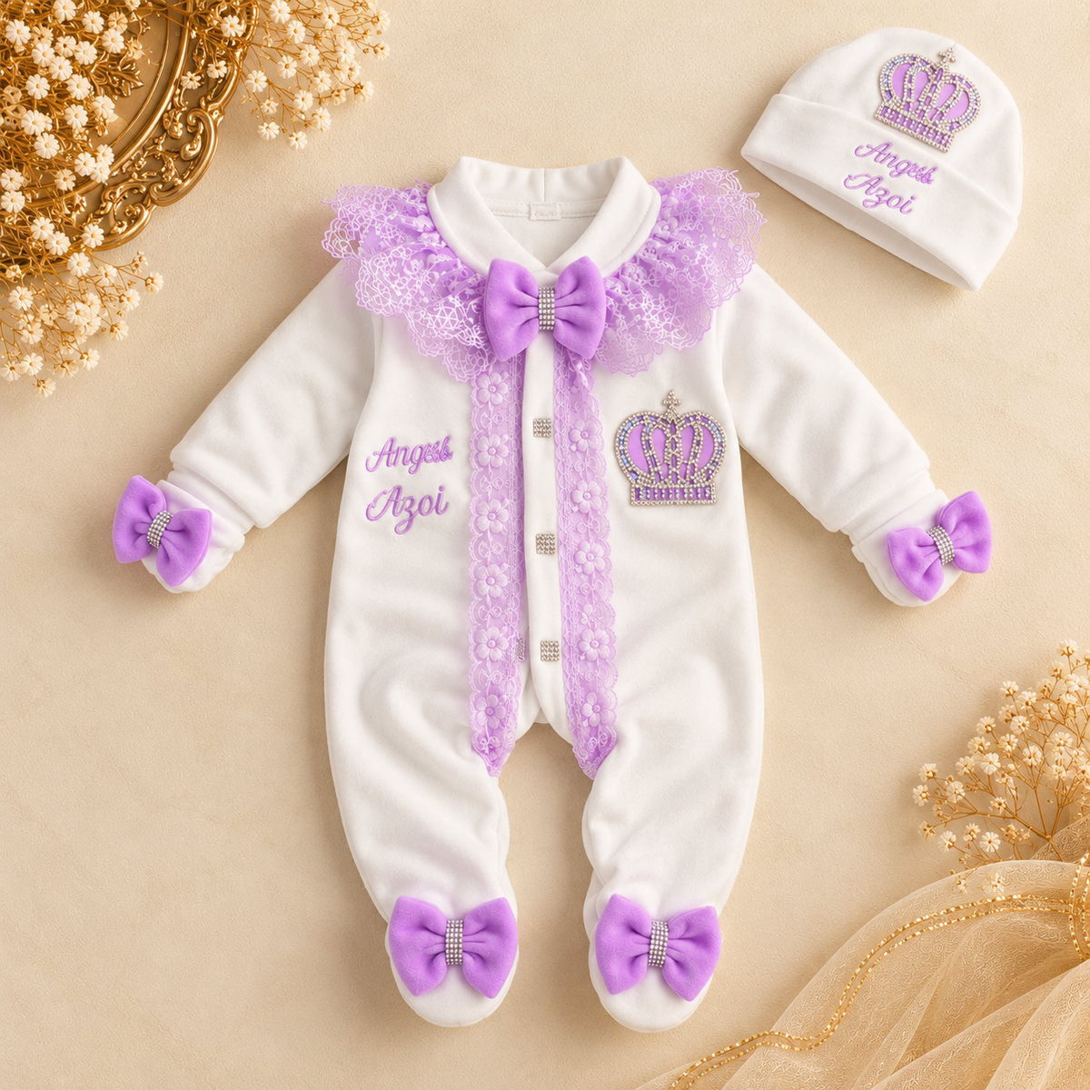 White baby footed onesie with purple lace trim, bows, and crown embroidery, shown with a matching beanie on a beige background with decorative dried flowers.