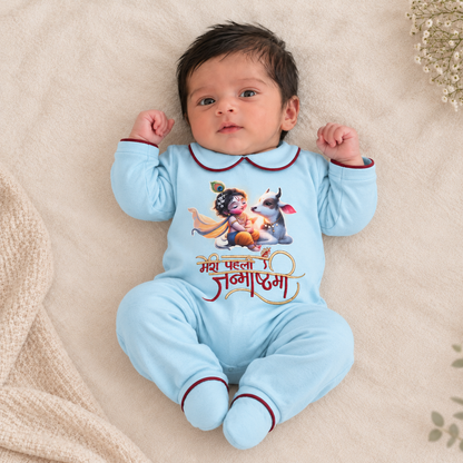 A baby lying on a soft beige blanket, wearing a light blue footed bodysuit with a colorful graphic of Krishna and a goat and Hindi text on the front.
