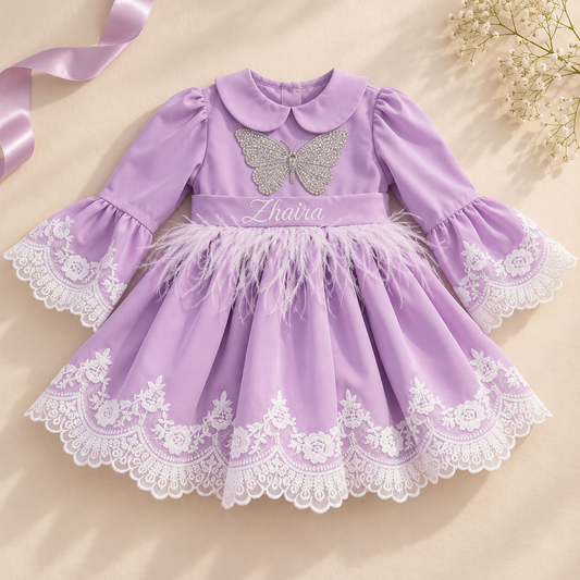 A baby girl's lavender purple dress with white lace trim, a glittery silver butterfly applique, and a feathered waistband, laid flat on a beige background with a pink ribbon and baby's breath flowers.