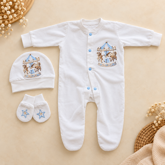 White baby footed sleeper with a snap closure and a blue and brown carousel embroidery on the chest, shown in a flat lay with a matching beanie and booties on a beige background.