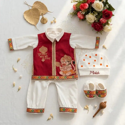A baby clothing set arranged in a styled flat lay on a light fabric background. The set includes a maroon and off white traditional outfit with colorful decorative borders and an elephant illustration, a white beanie with orange dots and the name 'Moksh', and white baby shoes with matching colorful trim.