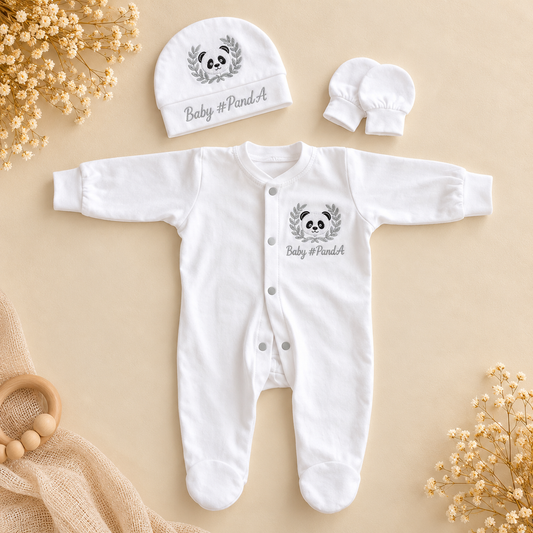 A white long-sleeve baby footed sleeper set with a matching bonnet and mittens, laid flat on a beige background. The sleeper and bonnet are printed with a gray panda face inside a leaf wreath and the text 'Baby #PandaA'.