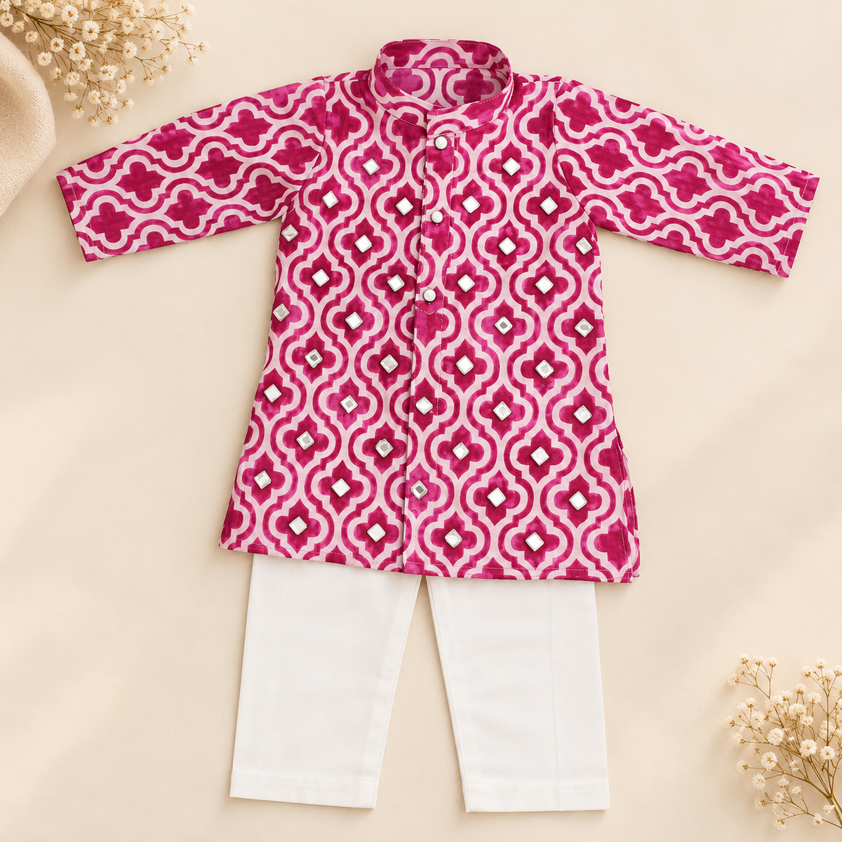 A baby boy's two-piece clothing set featuring a vibrant pink and white patterned kurta with a mandarin collar, paired with solid white pants, laid flat on a beige background with decorative dried flowers.