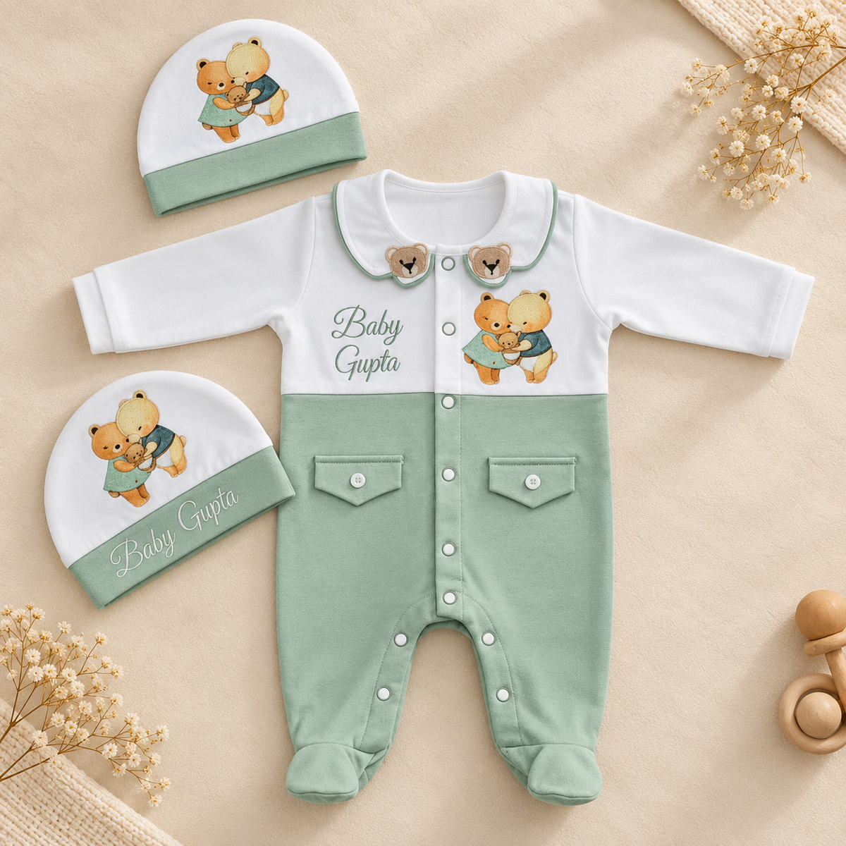A baby clothing set laid flat on a beige fabric background, including a long-sleeve footless romper and two matching beanies. The romper is white on the upper chest and collar, with mint green lower body and legs, snap closures, two front pockets, and teddy bear graphics with the text 'Baby Gupta.