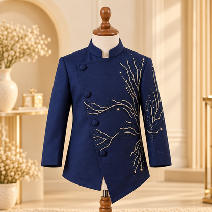 A navy blue men's jacket with gold embroidered branch patterns and button closure, displayed on a wooden mannequin in a warm, elegant interior setting.
