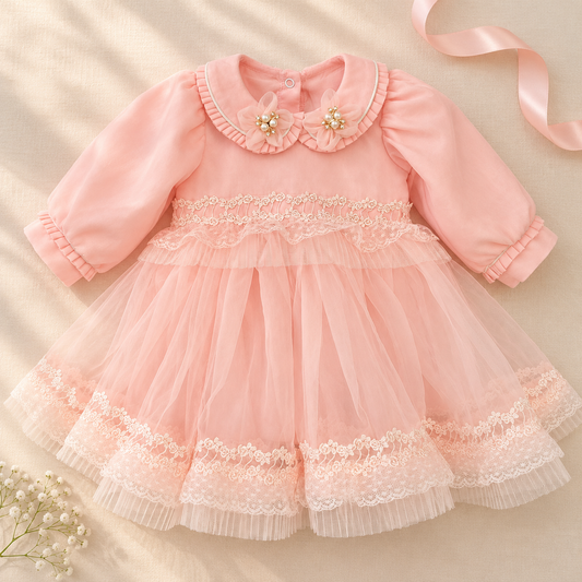 A baby girl's long-sleeve pink dress with a ruffled Peter Pan collar decorated with two pearl flower accents, a lace-trimmed bodice, and a layered tulle skirt with lace trim, laid flat on a beige fabric background with a pink ribbon and small white flowers.