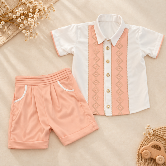 A baby boy's two-piece outfit set featuring a short-sleeve button-up shirt and matching shorts. The shirt is white with a vertical peach-colored front panel decorated with a geometric diamond pattern and gold-tone buttons.