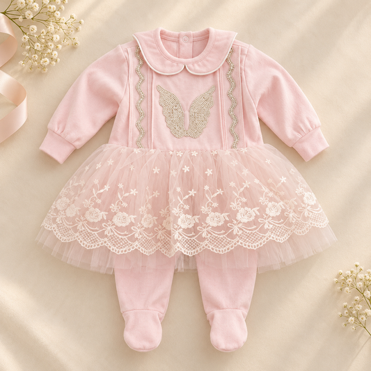 A baby girl's pink footed jumpsuit with a tulle tutu skirt, featuring embroidered angel wings on the chest and white floral lace trim on the skirt, laid flat on a beige fabric background with decorative baby's breath and ribbon.