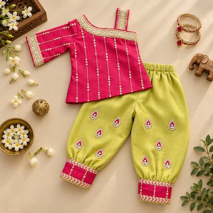 A traditional Indian outfit set featuring a bright pink top with gold embroidery and lime green pants with pink and gold accents, styled in a flat lay with decorative props.