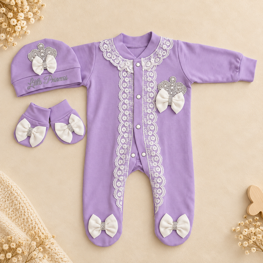 A baby footed sleeper in lavender purple with white lace trim, white bow details, and a matching bonnet, arranged on a beige background with small decorative flowers.