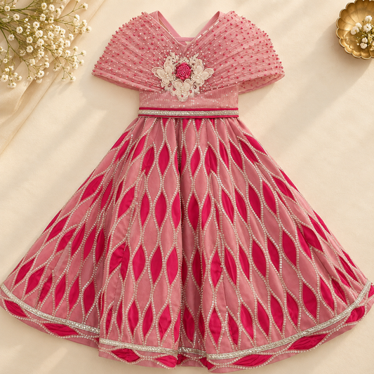 A pink traditional Indian dress for girls, featuring a V-neckline with a white and pink floral applique, a beaded waistband, and a flared skirt decorated with a pink and white geometric pattern.