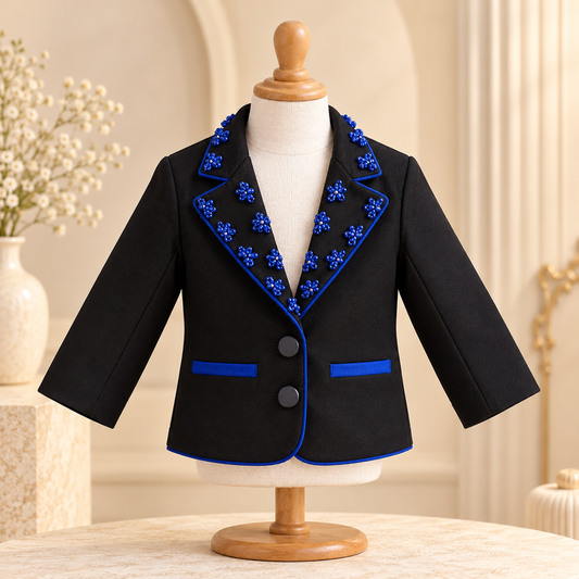 A black girls' blazer with bright blue floral embroidery and piping, displayed on a cream mannequin torso with a wooden stand.