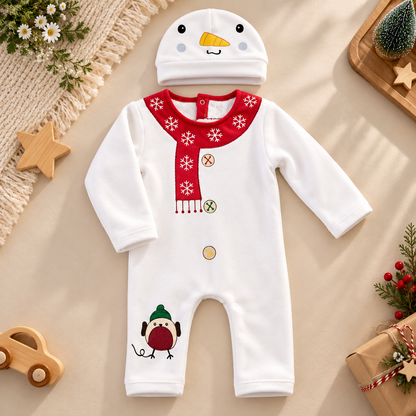 A baby snowman-themed one-piece romper and matching hat set, styled in a flat lay on a beige fabric background with holiday props including a small tree, wrapped gift, wooden stars, and a knitted textile.