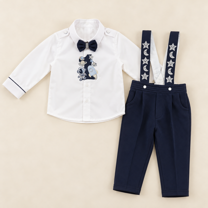 A baby boy's two-piece clothing set featuring a white long-sleeve button-down shirt with a navy bow tie and a space-themed graphic print, paired with navy blue pants with white star and moon suspenders, laid flat on a beige background.