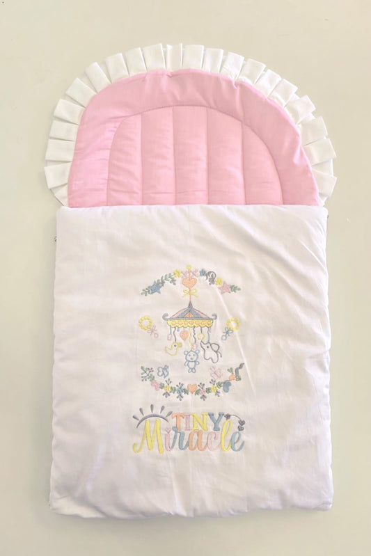 Baby sleeping bag with pink hood and carousel design on a beige background