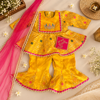A bright yellow traditional Indian outfit set with a peplum top, flared pants, and a pink dupatta, styled in a flat lay with decorative flowers, a woven hat, and a small card reading 'Shubh Deepawali'.