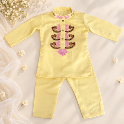 A baby's two-piece traditional outfit consisting of a long-sleeve top and matching pants in pale yellow. The top features a mandarin collar, buttoned front, and a decorative chest panel with pink and brown embroidered paisley patterns.